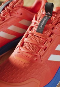 Sportowe buty w intensywnym czerwonym kolorze z białymi paskami, z chropowatą siateczkową cholewką i czarną metką oznaczoną napisem "CRAZYFLIGHT."
