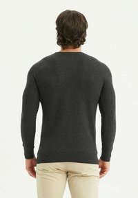 Pull gris foncé à col rond, avec des poignets et un ourlet côtelés, fabriqué à partir d'un tissu en maille texturée. Porté par-dessus un pantalon de couleur claire.