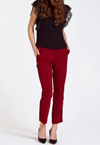 Top nero con maniche in pizzo a volant, abbinato a pantaloni slim-fit borgogna con strisce nere laterali e tasche. Tacchi alti neri.