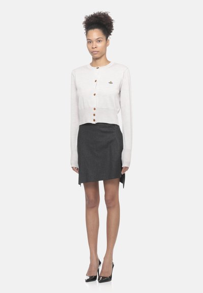 Cardigan accorciato beige chiaro con bottoni in legno, abbinato a una mini gonna grigia scura. Linee pulite e texture sottili nel tessuto.