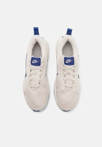 Baskets en maille blanche avec des accents bleus. Les caractéristiques incluent un système de laçage, un col rembourré et une languette à l'arrière. Logo Nike sur la languette.