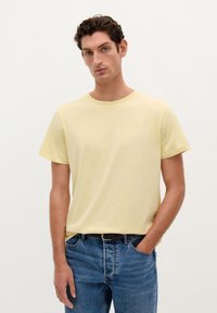 Lichtgele katoenen t-shirt met korte mouwen en een ronde hals, gecombineerd met blauwe denim jeans. Eenvoudig ontwerp, zonder zichtbare patronen of accenten.