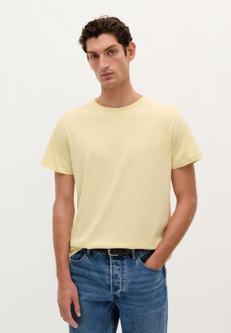Lichtgele katoenen t-shirt met korte mouwen en een ronde hals, gecombineerd met blauwe denim jeans. Eenvoudig ontwerp, zonder zichtbare patronen of accenten.