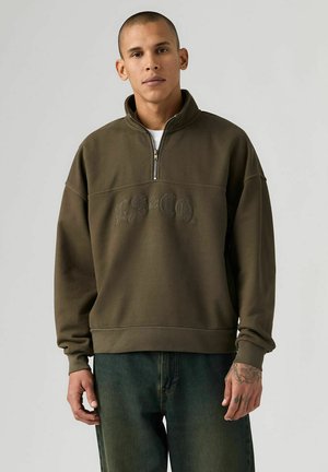 Sweatshirt med lynlås i olivengrøn, lavet af blødt materiale. Har høj krave, oversized pasform og broderet logo på tværs af brystet.
