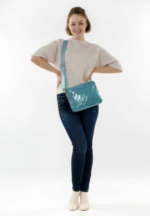 Un bolso cruzado acolchado en color azul agua, hecho de material brillante con una correa desmontable, que presenta una forma rectangular y un patrón geométrico.