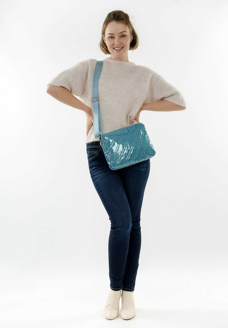 Un bolso cruzado acolchado en color azul agua, hecho de material brillante con una correa desmontable, que presenta una forma rectangular y un patrón geométrico.