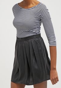 Randig svart- och vit långärmad topp med rund halsringning, kombinerad med en svart plisserad kjol med elastisk midja.