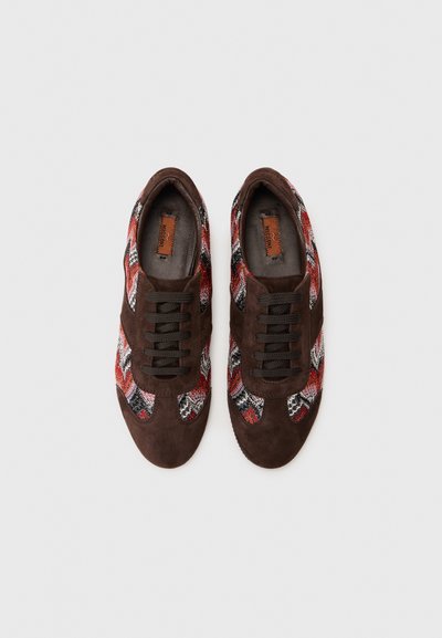 Baskets avec un dessus en daim marron et des côtés en textile à motifs colorés rouge, noir et blanc. Elles présentent des lacets noirs et une semelle intérieure beige.