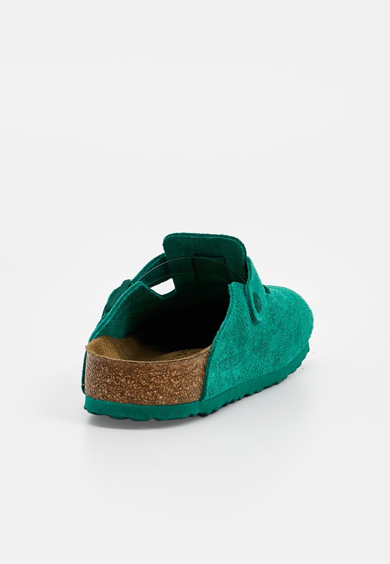 Zielone zamszowe buty wsuwane na korkowej podeszwie, o zaokrąglonym kształcie i pasku z tyłu dla wygody. Gładka faktura i minimalne detale hardware.