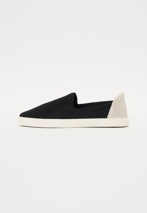 Svart slip-on sko med teksturert, ribbet overdel og en lysegrå semsket hæl-akzent. Har en hvit gummisåle, designet for fritidsbruk.