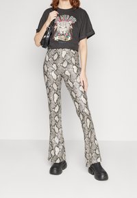 Svart t-shirt med leoparddesign, kombinerad med högmidjade, utsvängda byxor med ett beige och svart ormskinnstryck. Svarta plattformsskor.