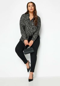 Long-sleeve black blouse with a leaf pattern, paired with black leggings and pointed-toe heels; holding a small black handbag.