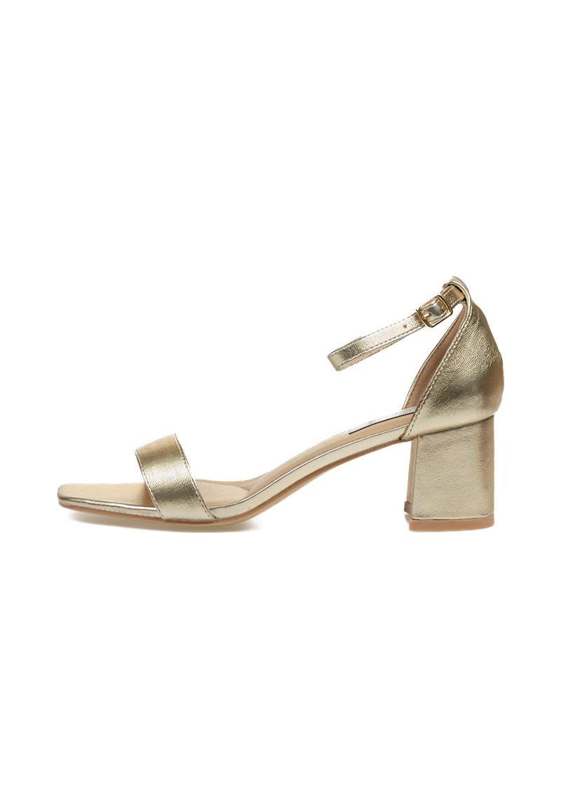 Sandalia de tacón bloque metálico dorado con tira en el tobillo, punta abierta, correas mínimas, textura suave y un ribete de plástico transparente en la suela.