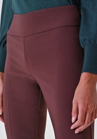 Leggings bordeaux a vita alta realizzati in un tessuto morbido ed elastico. Presentano una cintura larga e dettagli delle cuciture verticali lungo i lati.