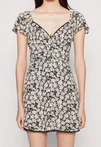 Robe noire courte avec un motif floral en blanc et crème. Le design comprend des manches courtes et un décolleté en V avec un lien décoratif.