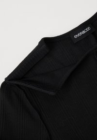 Zwarte geribde stof top met een ronde halslijn en een label met "even&ODD." Bevat textuurdetails langs de randen.