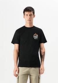 Sort bomulds t-shirt med korte ærmer, der har et farvet logo på venstre bryst og en glat, jævn tekstur.