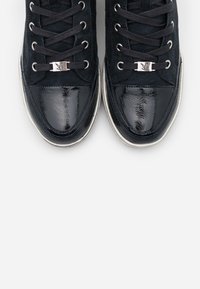 Marinblå sneakers med ovandel i mocka och glansig lacklädertå. Utrustad med platta svarta snören och en silvermetallaccent i snörningen.