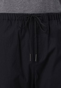 Shorts noirs avec taille élastique en tissu texturé, dotés d'un cordon de serrage avec des embouts en métal et d'un haut gris partiellement visible au-dessus.