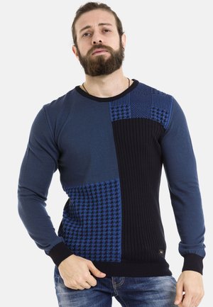 Blauer Pullover mit strukturierten Patches in zwei Farbtönen, ausgestattet mit gerippten Abschnitten und einem Hahnentrittmuster. Lange Ärmel und Rundhalsausschnitt.
