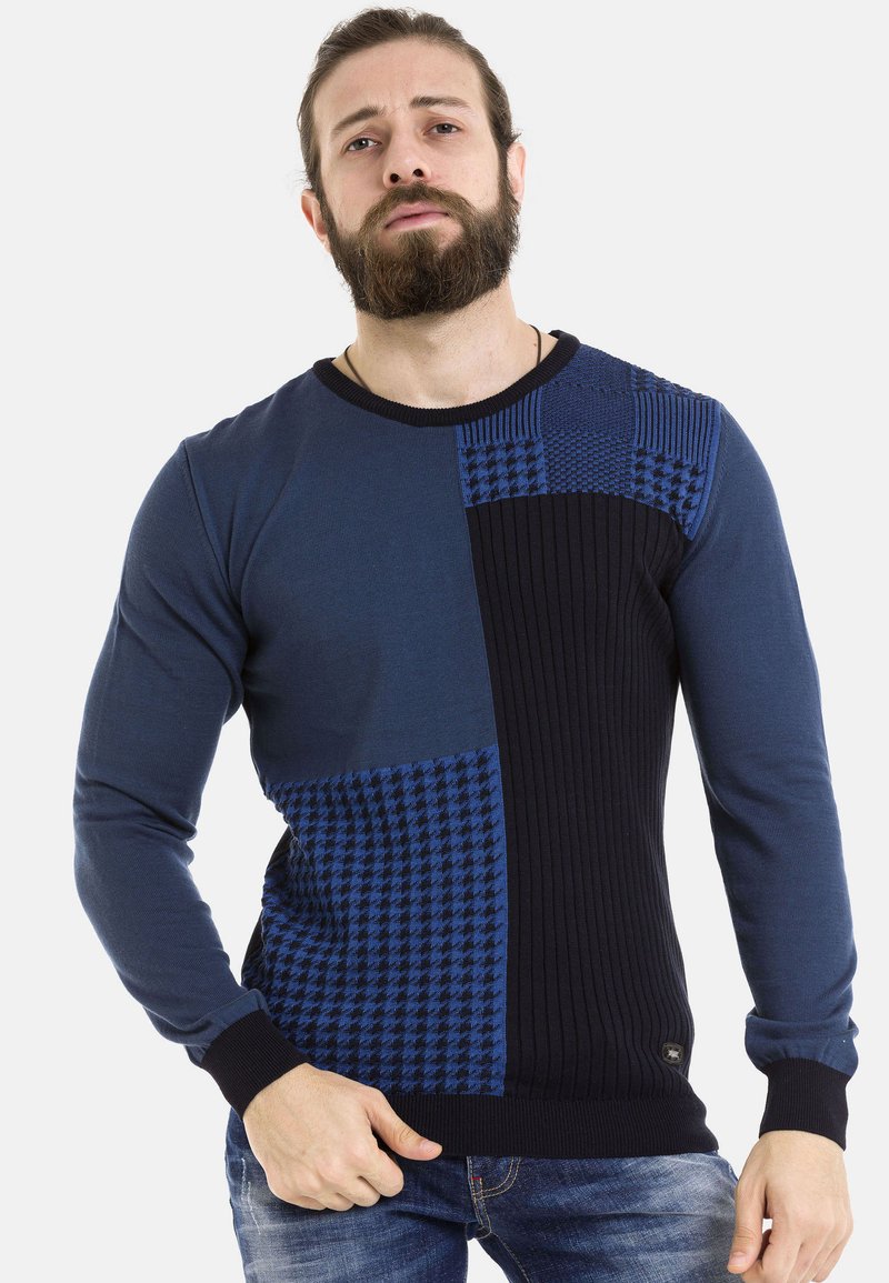 Blauer Pullover mit strukturierten Patches in zwei Farbtönen, ausgestattet mit gerippten Abschnitten und einem Hahnentrittmuster. Lange Ärmel und Rundhalsausschnitt.