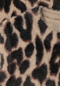 Gros plan d'un tissu doux et duveteux avec des taches imprimées léopard noires et brunes sur un fond beige, montrant la texture et les détails du tricot.