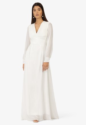 Long white dress with a deep V-neckline, pleated bodice, and sheer long sleeves. Flowing fabric extends to the floor. Simple, elegant design.