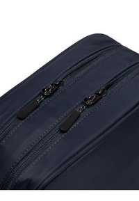 Námorníckomodrá látková taška s dvoma čiernymi zipsami a textúrovanými ťahadlami, so hladkým povrchom a odolným šitím pozdĺž okrajov.