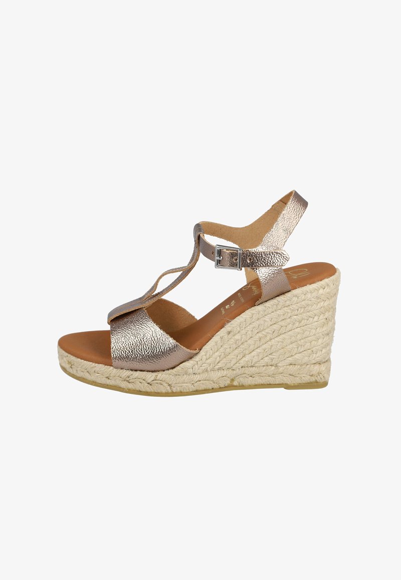 Sandalias de cuña con un upper texturizado metálico, correa ajustable en el tobillo y una suela cubierta de cuerda natural. La plantilla marrón complementa el diseño.