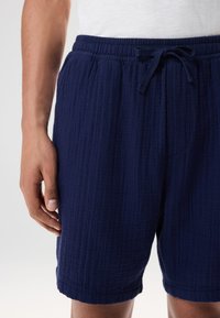Donkerblauwe, gestructureerde korte broek met een elastische tailleband en trekkoord. Heeft een ontspannen pasvorm en valt boven de knie.