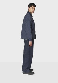 Marineblå polstret jakke med høj krave, parret med mørk denim brede bukser og sorte sko. Har en tekstureret overflade og sidelommer.