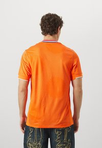 Chemise orange à manches courtes avec un motif à pois, bordure de col blanche et accent bleu contrastant. Tissu léger et respirant.