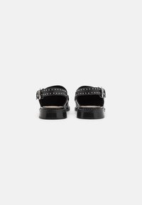 Black sandals with back heel strap, studded accents along the strap, flat sole, and a shiny leather finish. Minimalist design with adjustable buckle.