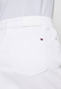 Pantalones cortos de mezclilla blanca con un parche de cuero de TOMMY HILFIGER en la cinturilla. Presenta un bolsillo trasero con un pequeño acento de logo en rojo, blanco y azul.