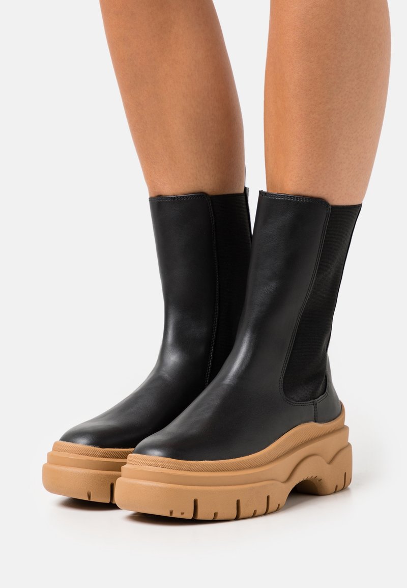 Zwarte leren enkellaarzen met elastische zijkanten en dikke beige rubberen zolen met een gemarmerd loopvlak.