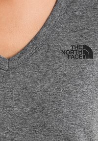 Szara koszulka z dekoltem w serek wykonana z miękkiej bawełnianej mieszanki, z czarnym logo The North Face nadrukowanym po lewej stronie klatki piersiowej.