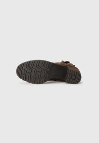 Bota de piel marrón con parte superior de ante texturizado, suela de goma con un patrón de zigzag, equipada con una cremallera lateral para facilitar el uso.