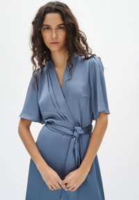 Blaues Wickelkleid aus strukturiertem Stoff mit kurzen Ärmeln, tailliert. Verfügt über einen V-Ausschnitt und ein glattes, fließendes Design.