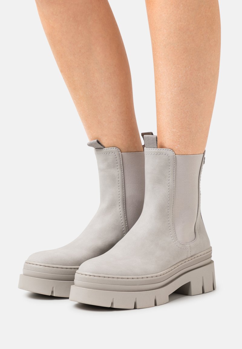 Light gray ankle boots made of suede with elastic side panels, thick platform soles, and rounded toes. Rubber tread accents on the sole.