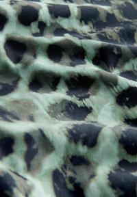 Textil mit einem grünen und schwarzen Leopardenmuster; zeichnet sich durch eine weiche Textur und fließenden Stoff mit unterschiedlich großen Flecken und weichen Kanten aus.
