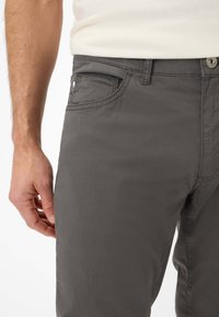 Grijze katoenen broek heeft een recht model met zijzakken en contrasterende stiksels. De stof lijkt glad met een minimale textuur.