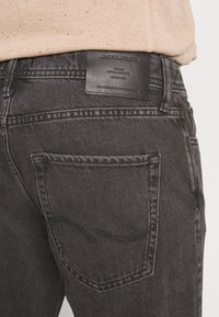 Mustad denim teksad, millel on tekstuuriline pind, sisaldades nahast logo silti ja tagatasku õmblust veidi heledamas toonis.