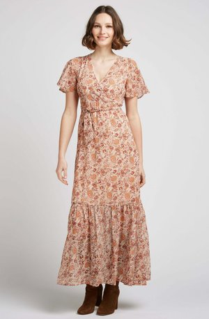 Robe maxi en tissu léger avec un imprimé floral dans des tons chauds, décolleté en V, manches courtes à volants et jupe à volants. Portée avec des bottes marron.