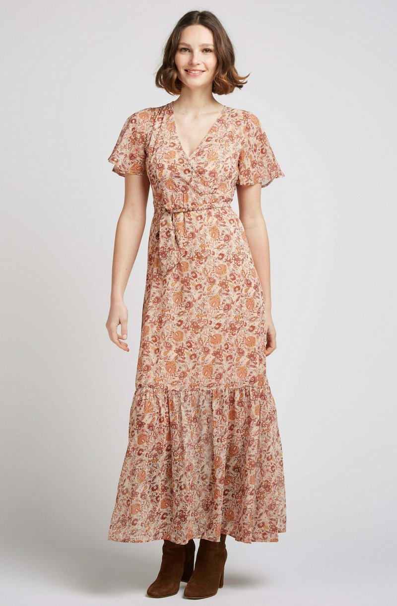 Robe maxi en tissu léger avec un imprimé floral dans des tons chauds, décolleté en V, manches courtes à volants et jupe à volants. Portée avec des bottes marron.