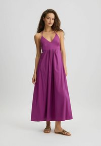 Maxi dress in vibrant magenta, with a fitted bodice, deep V-neck, and gathered waist. Worn with leopard print slide sandals.