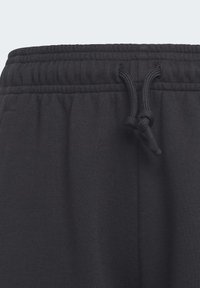 Pantalones de chándal negros con cinturilla elástica y cordón ajustable. La tela tiene una textura suave y parece ligera.