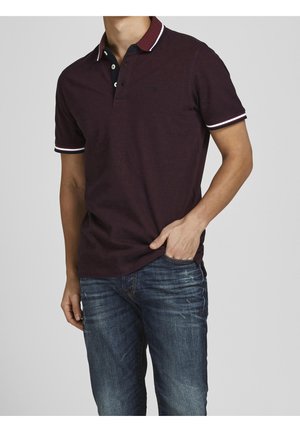 Burgunderrotes Polohemd mit navyfarbenem Kragen und weißen Akzenten, aus Baumwolle. Getragen mit blauen Jeans aus Denim, die ein leicht tailliertes Design aufweisen.