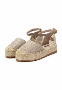 Sandalias espadrilles con tela tejido en beige y suela de yute. Presentan una punta redondeada y correas ajustables en el tobillo con una suela plana y texturizada.