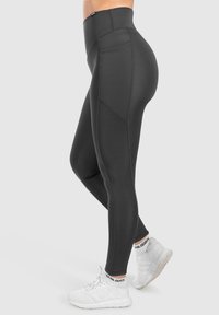 Leggings neri a vita alta in tessuto elastico, con una tasca laterale e un design a pannelli. Abbinati a scarpe da ginnastica bianche.