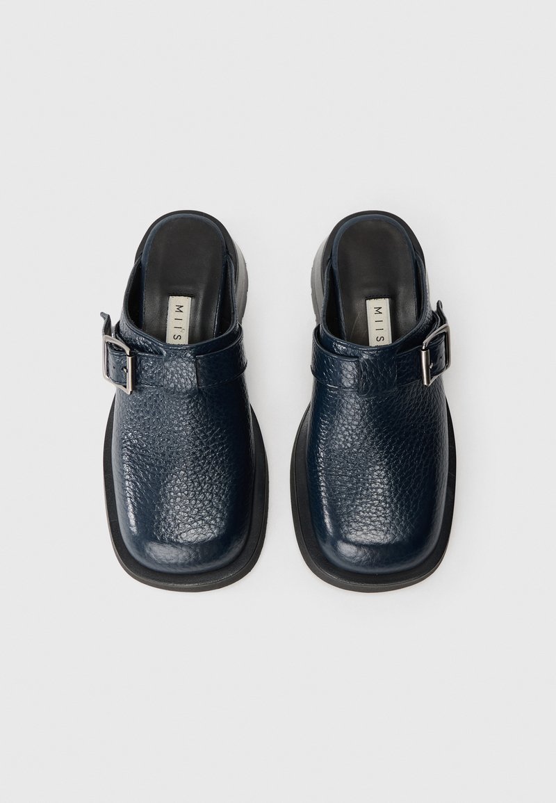 Marineblaue Lederclogs mit strukturiertem Obermaterial, Schnallenakzent und dicker schwarzer Sohle, mit offenem Fersenanschnitt und gepolsterter Innensohle.